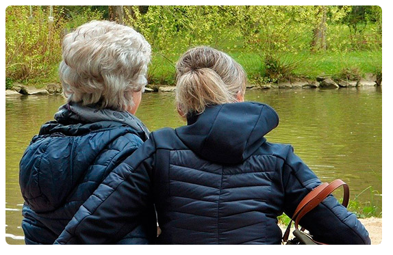 Dos mujeres de espalda delante de un río. La joven le pasa el brazo a la mujer mayor.