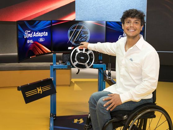Hombre usuario de silla de ruedas, delante de una pantalla que tiene incorporado un volante para jugar.