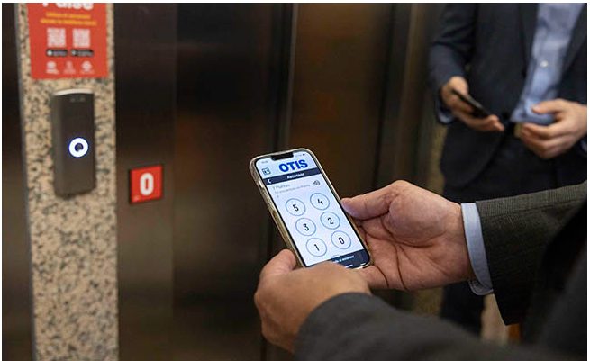 Persona utilizando la app Pulse en su móvil delante de un ascensor